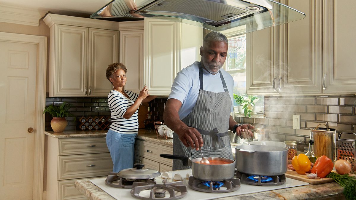 Older couple cooking on a natural gas stove in a bright home kitchen.