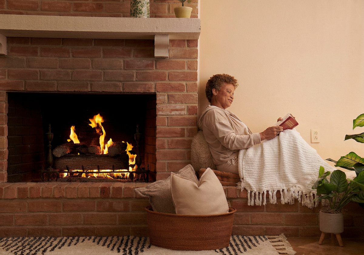 Woman sitting near a warm natural gas fireplace at home.